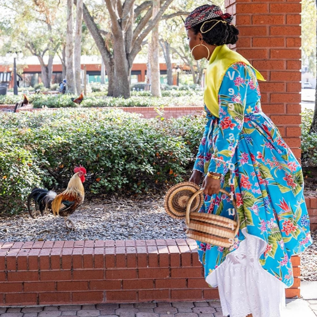 A woman wearing a Blue Floral Wob Dwiyet,  and a yellow foula is looking at a rooster.