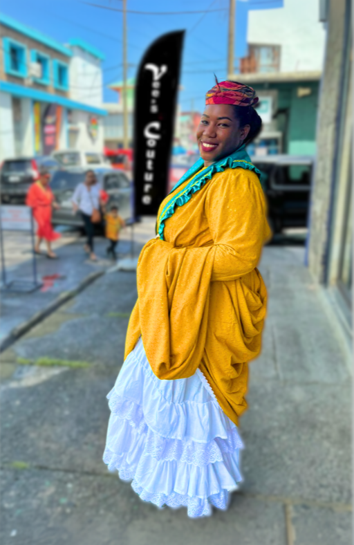  A woman wearing a vibrant gold Wob Dwiyet, a white petticoat and a contrasting tete Ale headpiece. She exudes elegance and confidence as she smiles at the camera