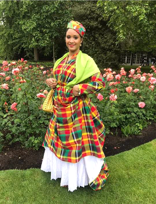 A young lady wearing a Madras Wòb Dwiyèt with bright green foula. She is in a flower garden.